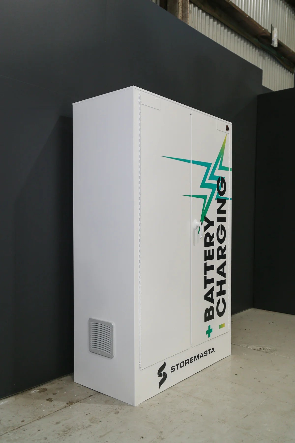 A white battery charging cabinet with green and black branding on the front, including a lightning bolt and the text 'BATTERY CHARGING'. The cabinet has a door with a handle on the side and a visible fire suppression system.