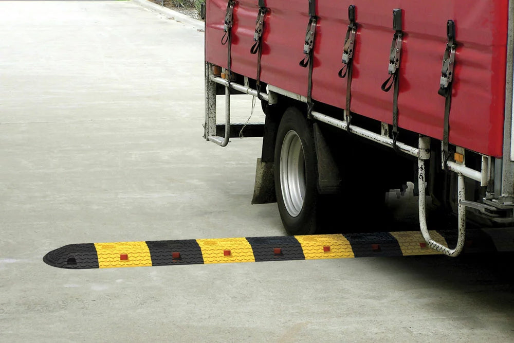 Red truck with a trailer on a road next to a yellow and black speed bump.