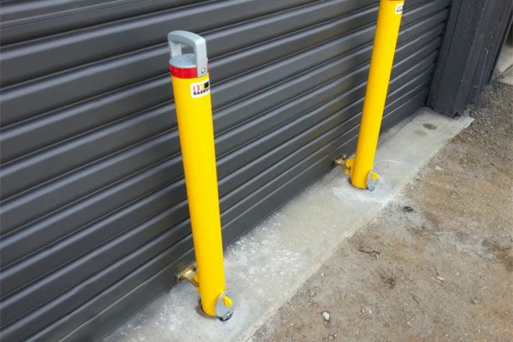 Two yellow bollards with red and white labels against a gray metal garage door.