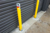 Two yellow bollards with red and white labels against a gray metal garage door.