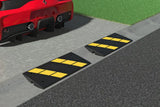 Two speed bumps with yellow stripes on a road next to a red car.